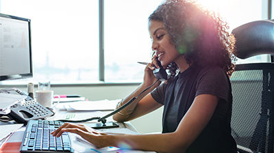 Applied Marketing Automation A woman sitting at her desk and talking on a telephone while typing on her keyboard